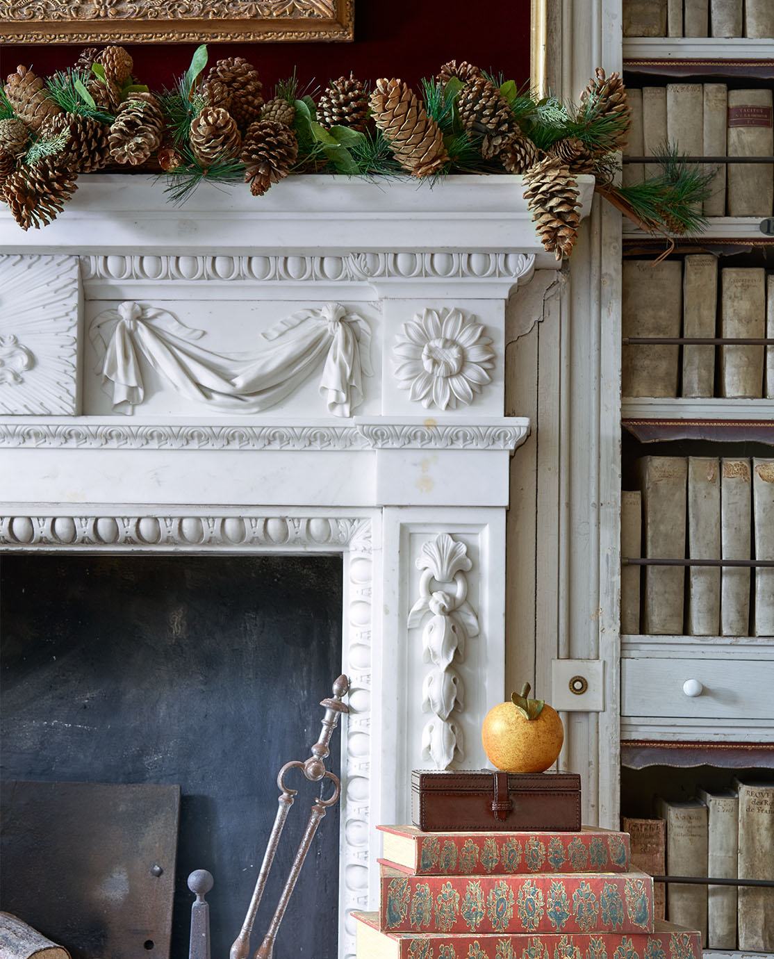 The corner of a white stone mantel decorated with ferns and greenery, next to an antique bookshelf.