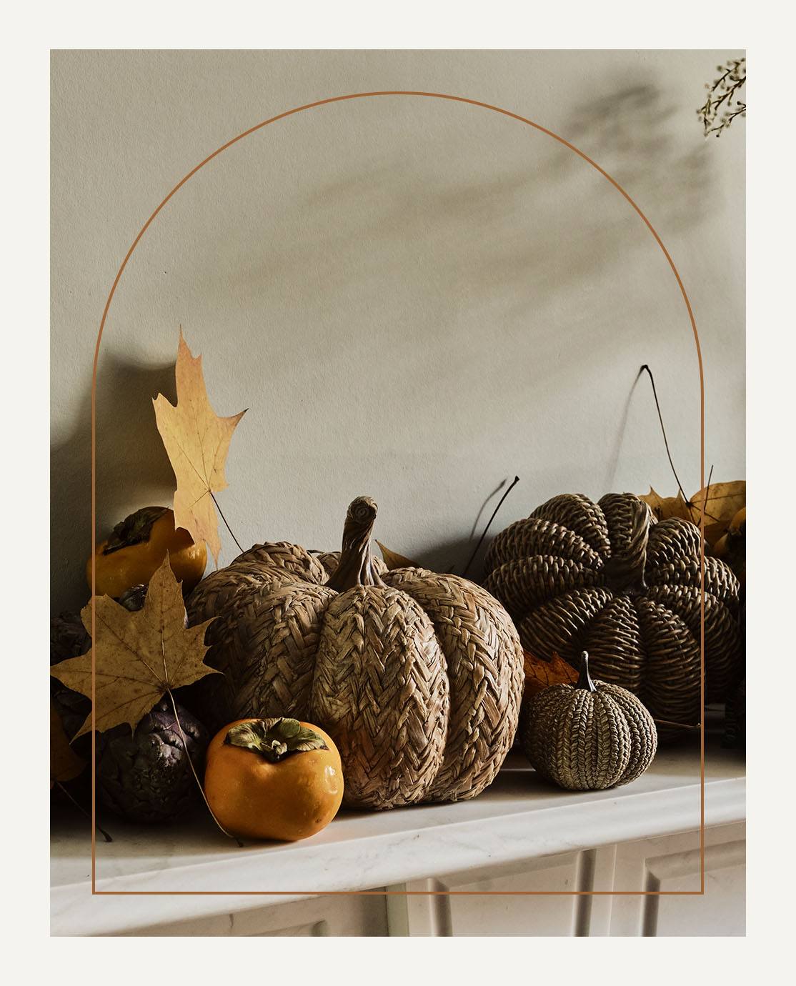 A fall display of pumpkins and leaves decorates a white mantel.