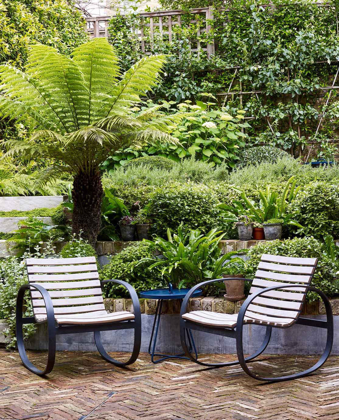 Two wooden garden chairs on a stone herringbone patio.