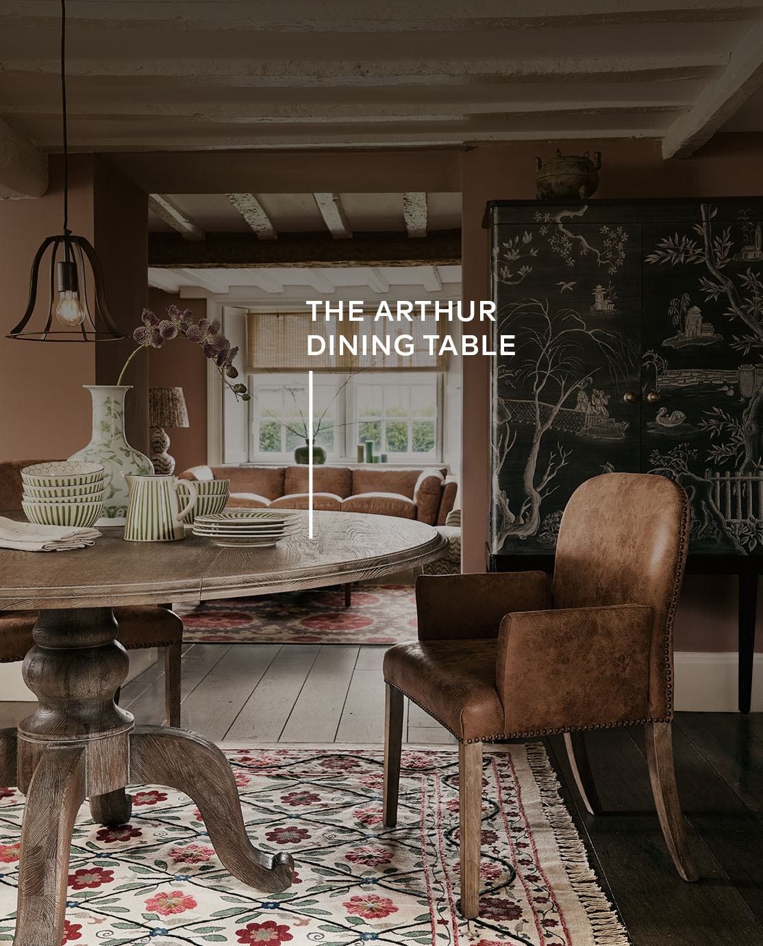 An autumnal setting featuring a large round wooden dining table and leather dining chairs in a lowly lit cottage dining room.