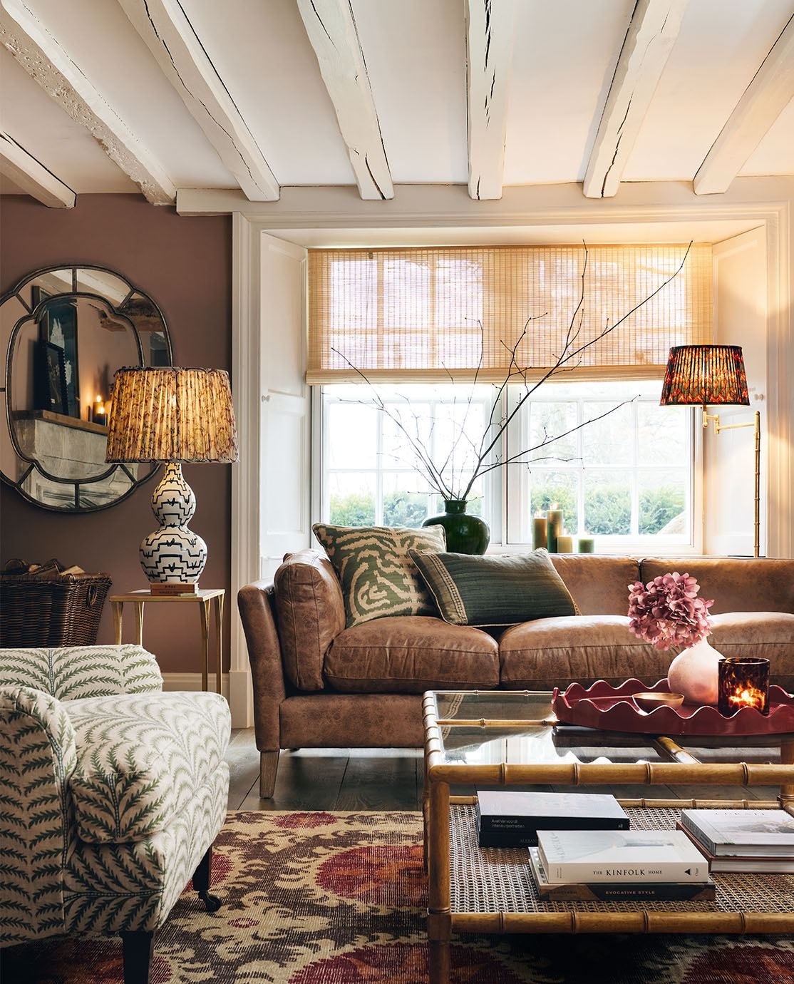 A cottage sitting room with two sofas, a coffee table and a rug, two lamps and a mirror, in front of a large window.