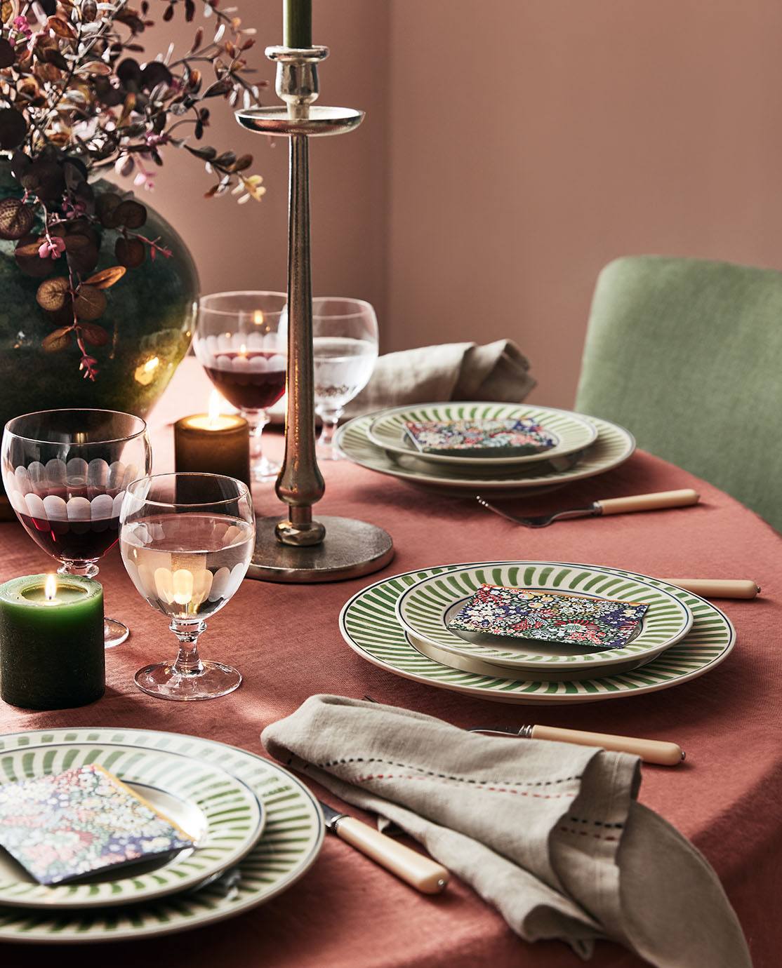 An autumnal tablescape with green-and-white striped crockery, white cutlerty and a red tablecloth.