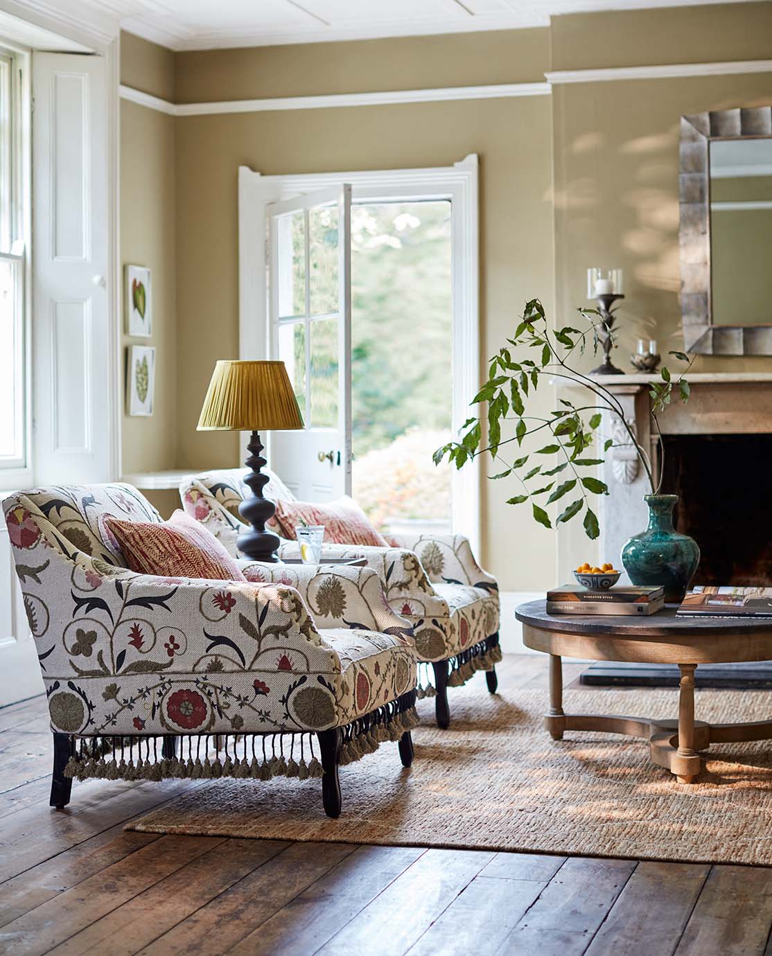 A sitting room setting with embroidered armchairs, a yellow pleated lampshade and a jute rug