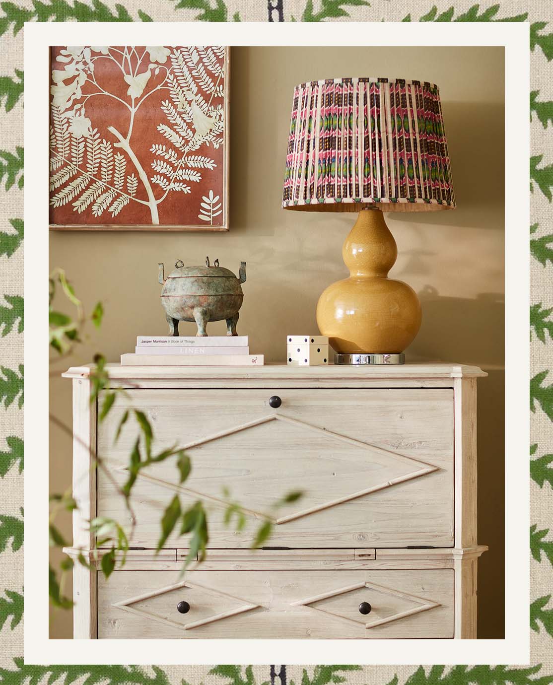 A grey cabinet is decorated with a yellow lamp and colorful pleated shade