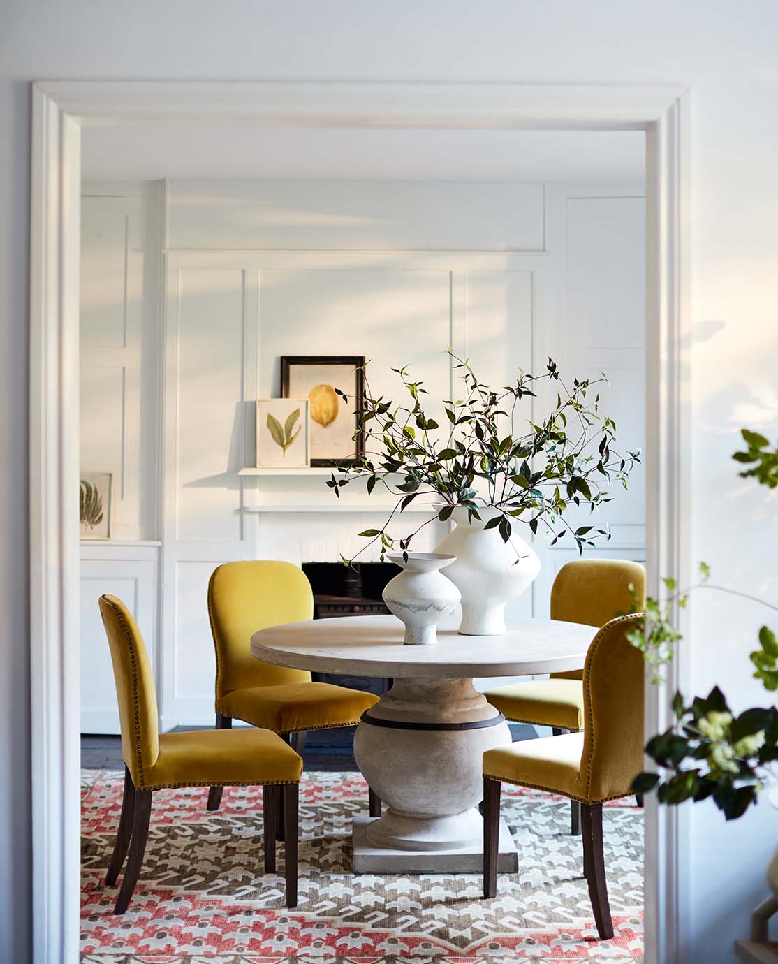 A dining room setting with a round, stone table, four yellow velvet dining chairs and a red patterned rug