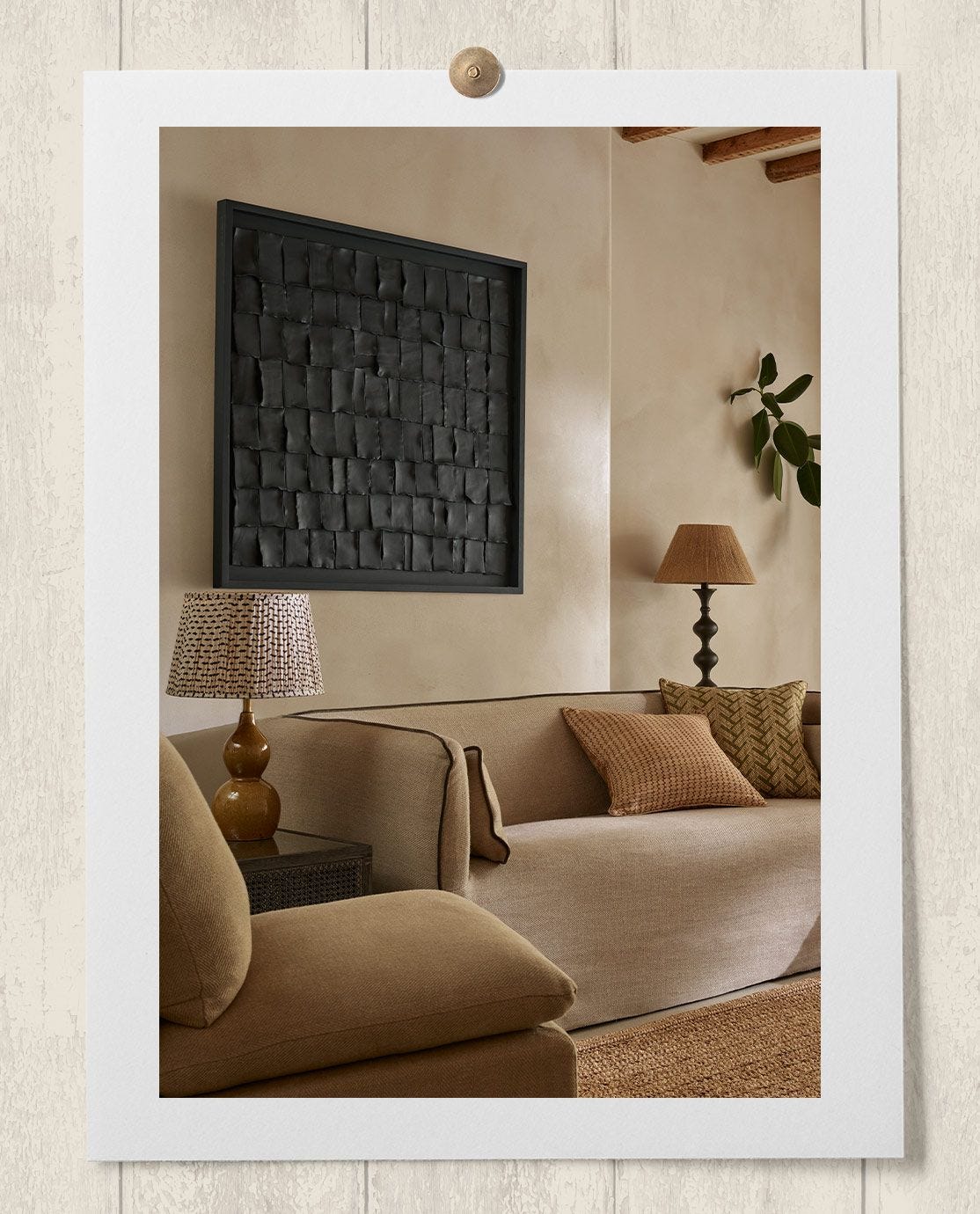 A wall art created from sheets of black clay hangs above a beige linen sofa
