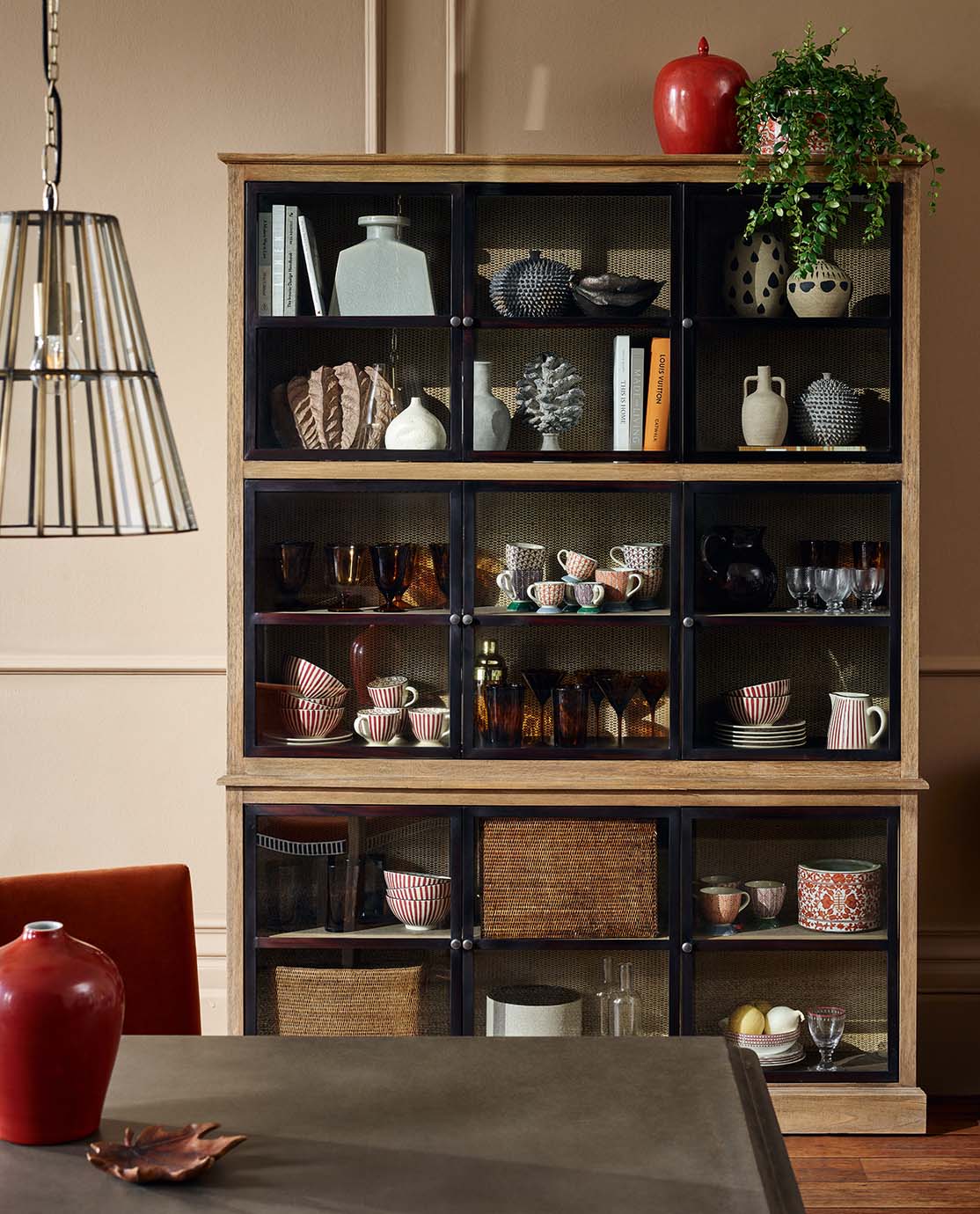 A wooden cabinet filled with crockery, cookbooks and ornaments. 