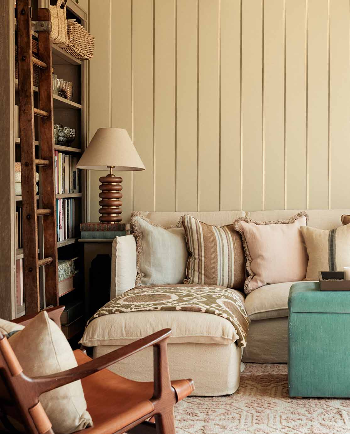 A sitting room setting with white paneled walls, a linen-covered L-shaped sofa and wooden bookcases