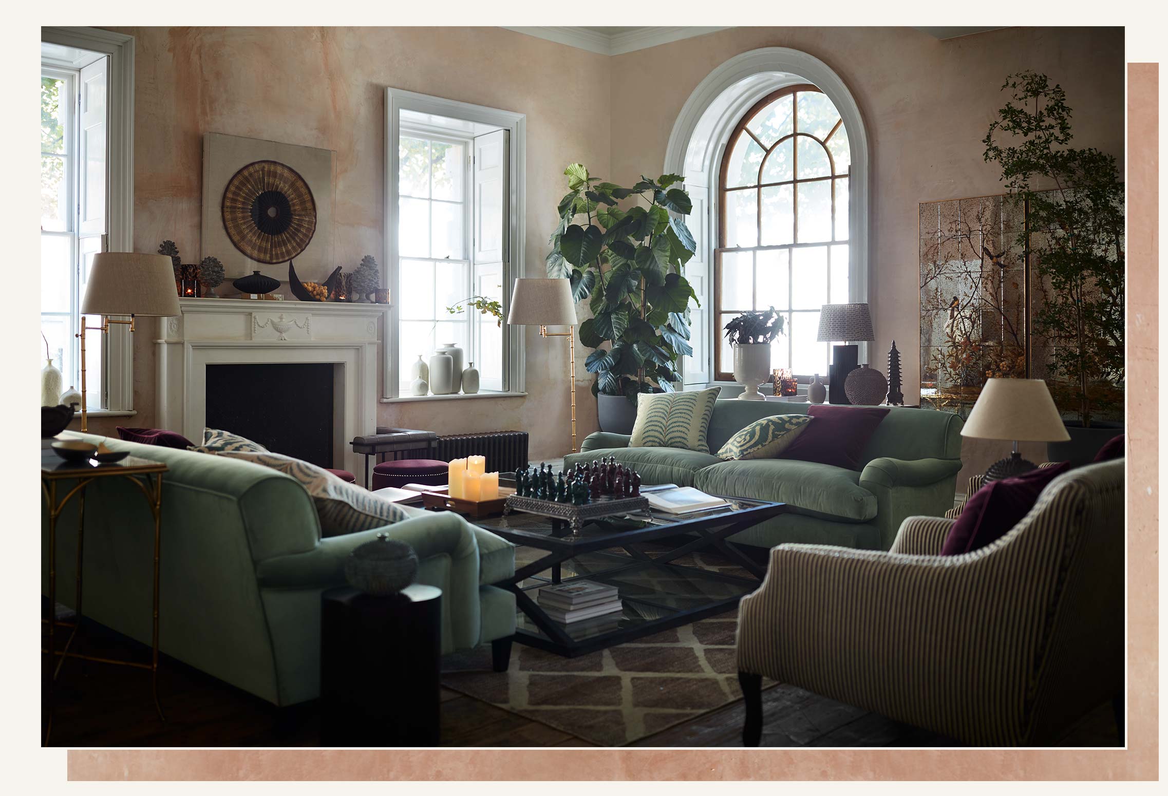 A sitting room setting, with light blue sofas, a black and glass coffee table and a brown rug. The walls are plastered and there is a large arched window in the background.