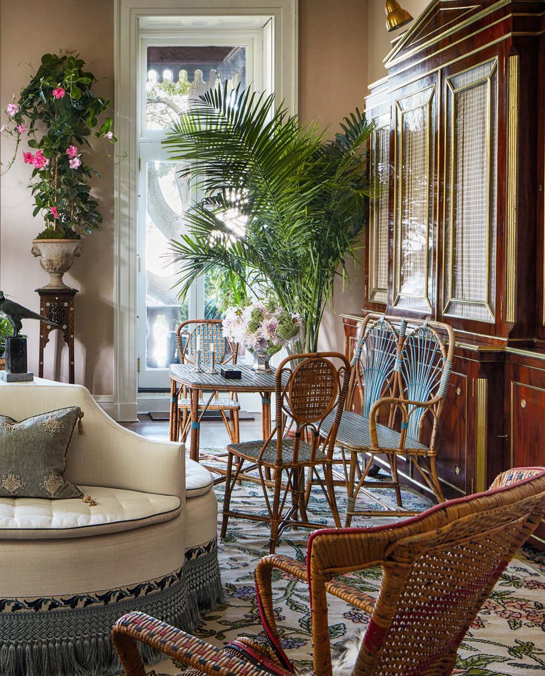 A reception room in Adam Lippes's home, which is decorated with antique wooden and rattan furniture and a floral rug.