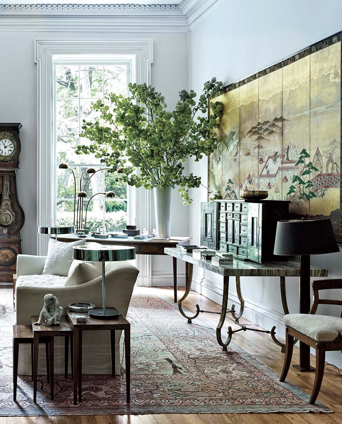 The corner of a mantelpiece decorated with a vase, a mirror and flowers. Three botanical prints hang on the wall next to it.