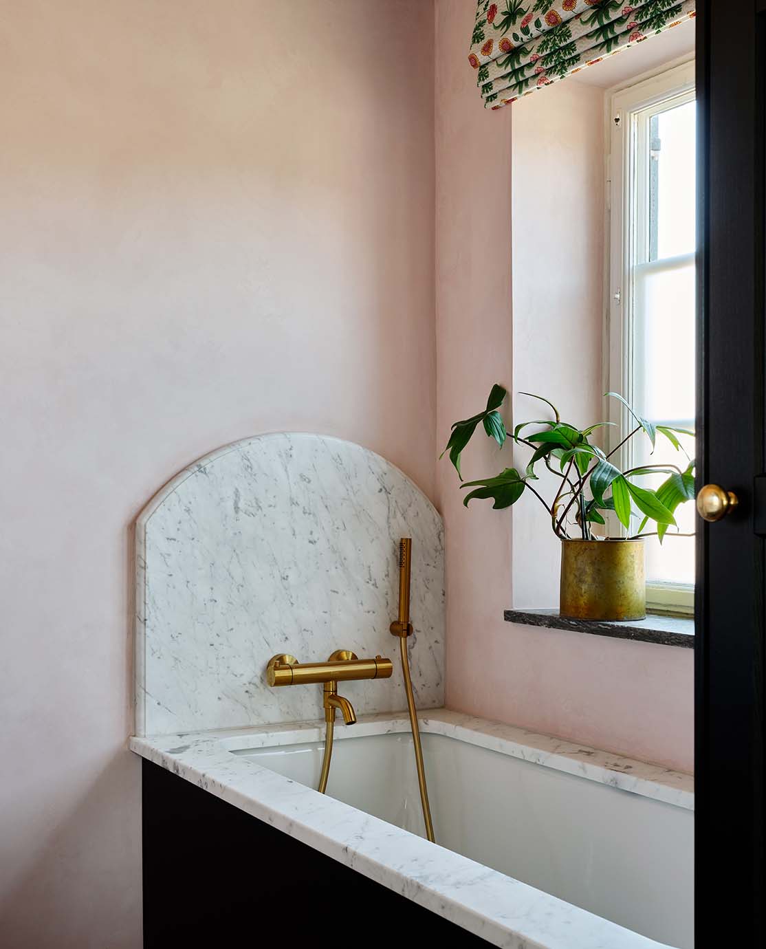 A marble and navy blue bath tub in a light pink bedroom.