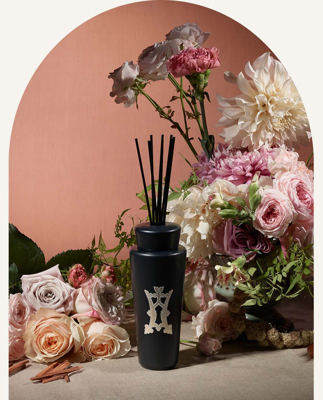 A black diffuser sits in front of a bouquet of pink flowers and a pink backdrop