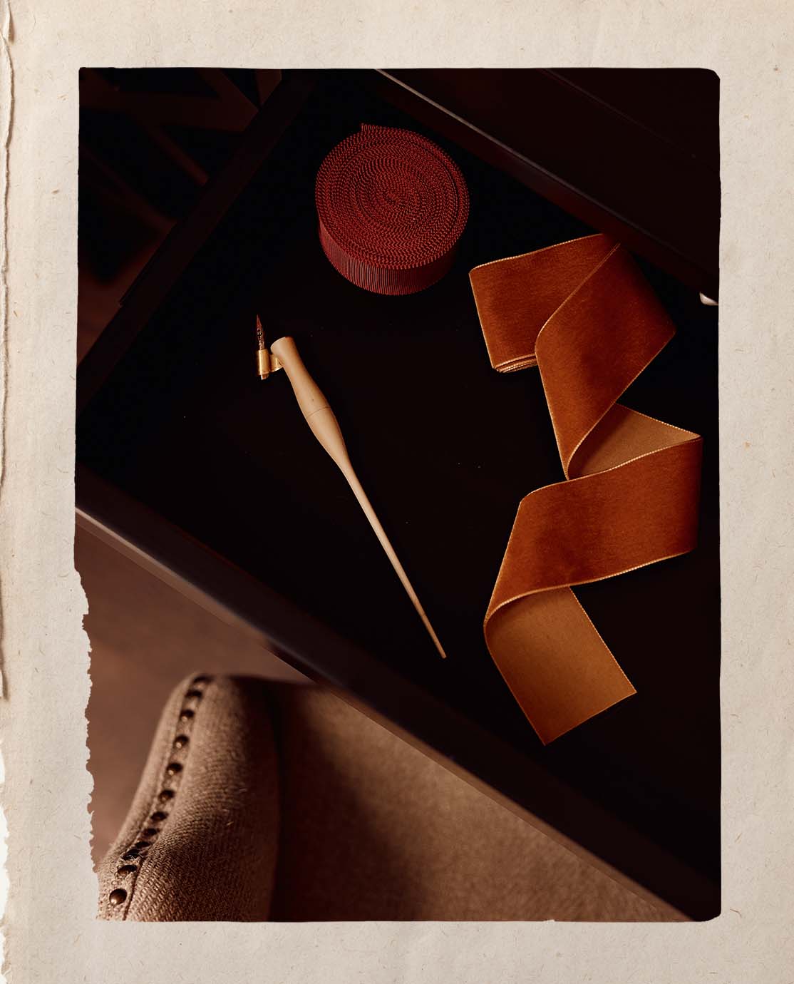 An aerial shot of a calligraphy pen and a reel of rust-colored velvet ribbon on a black desk