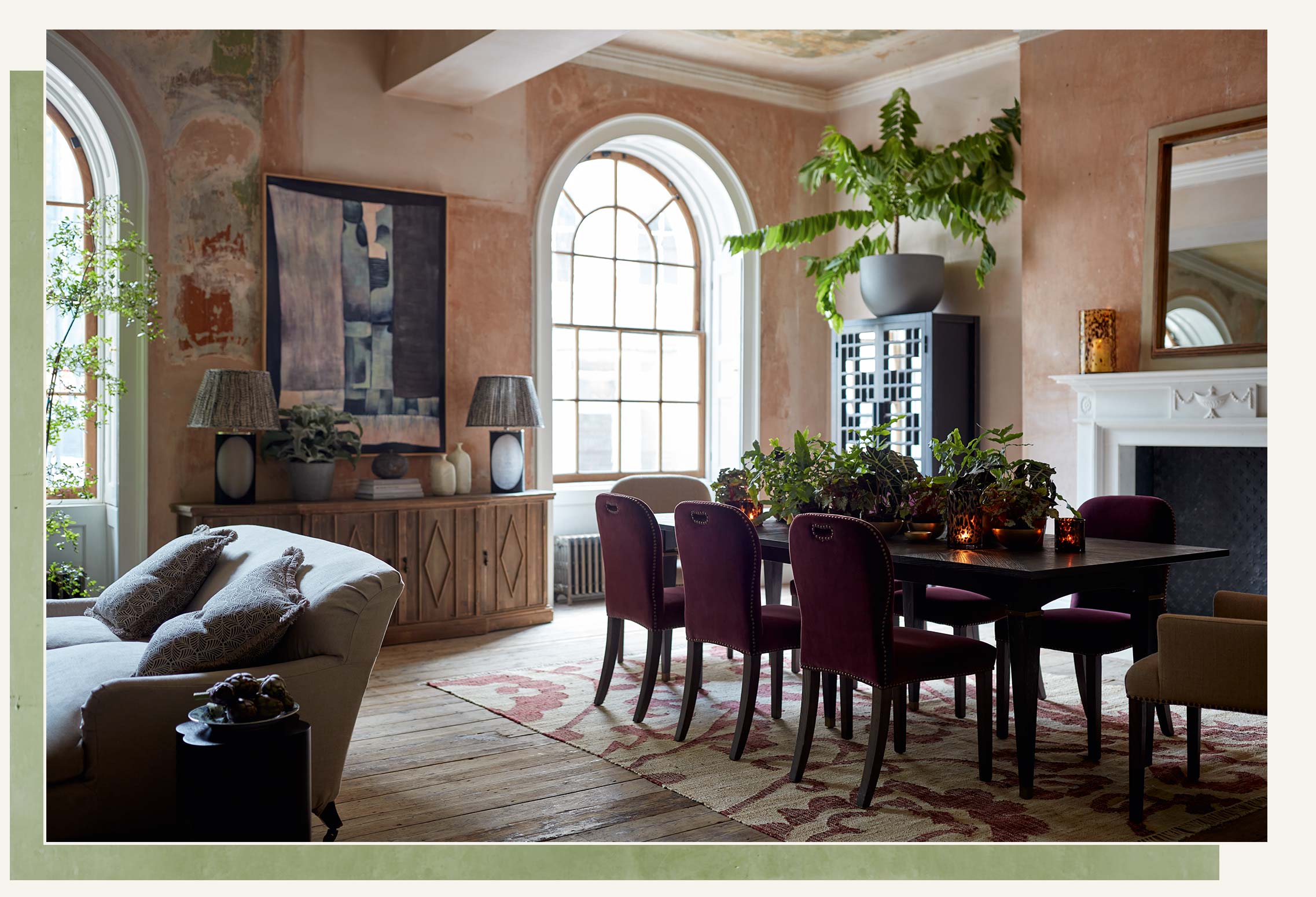 A large black dining table and red velvet chairs sit on top of a patterned rug in a heritage building.