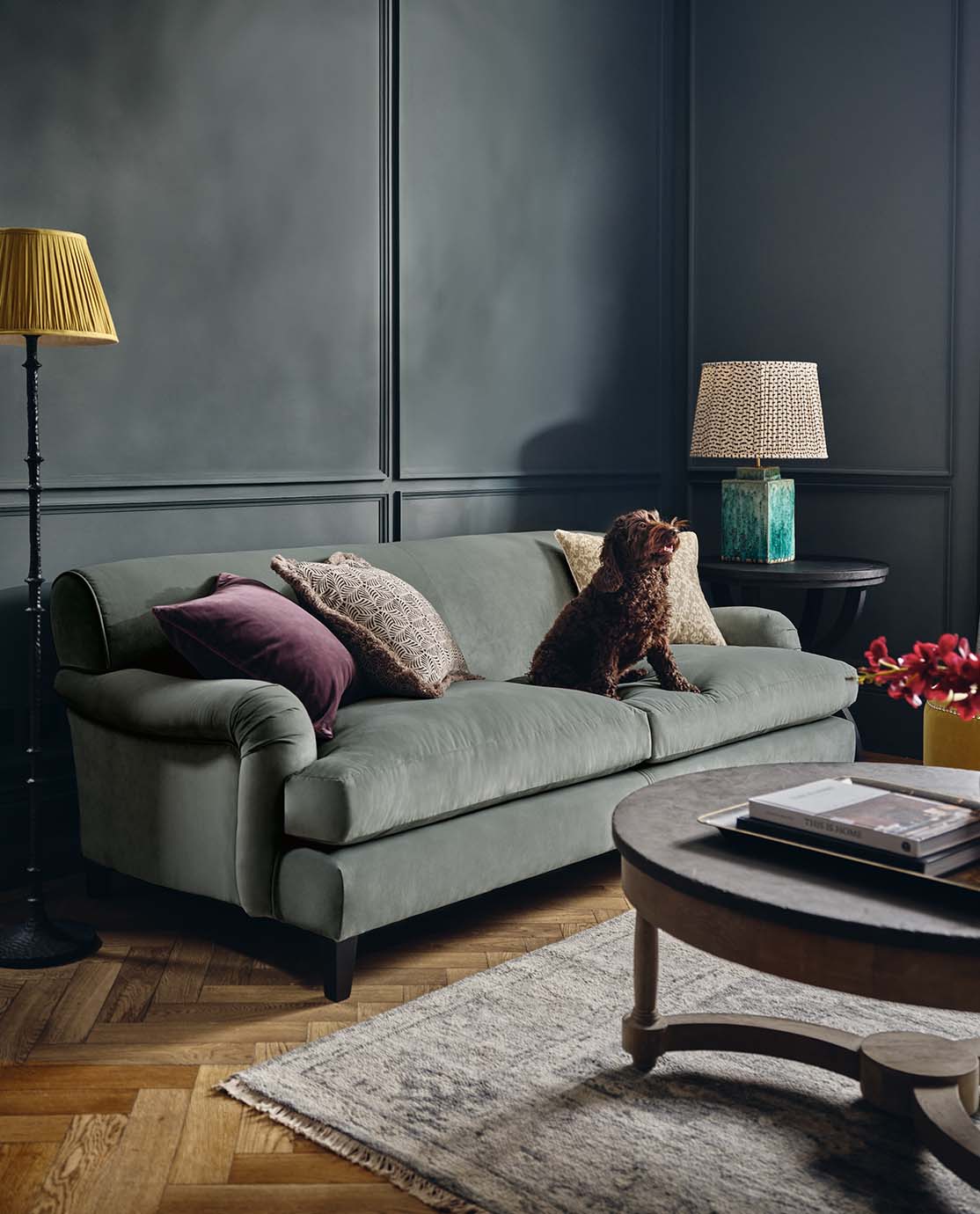 A red Clever Velvet sofa, decorated with a printed pillow. A breakfast tray holding a crossiant and cup of tea sit on top of it.