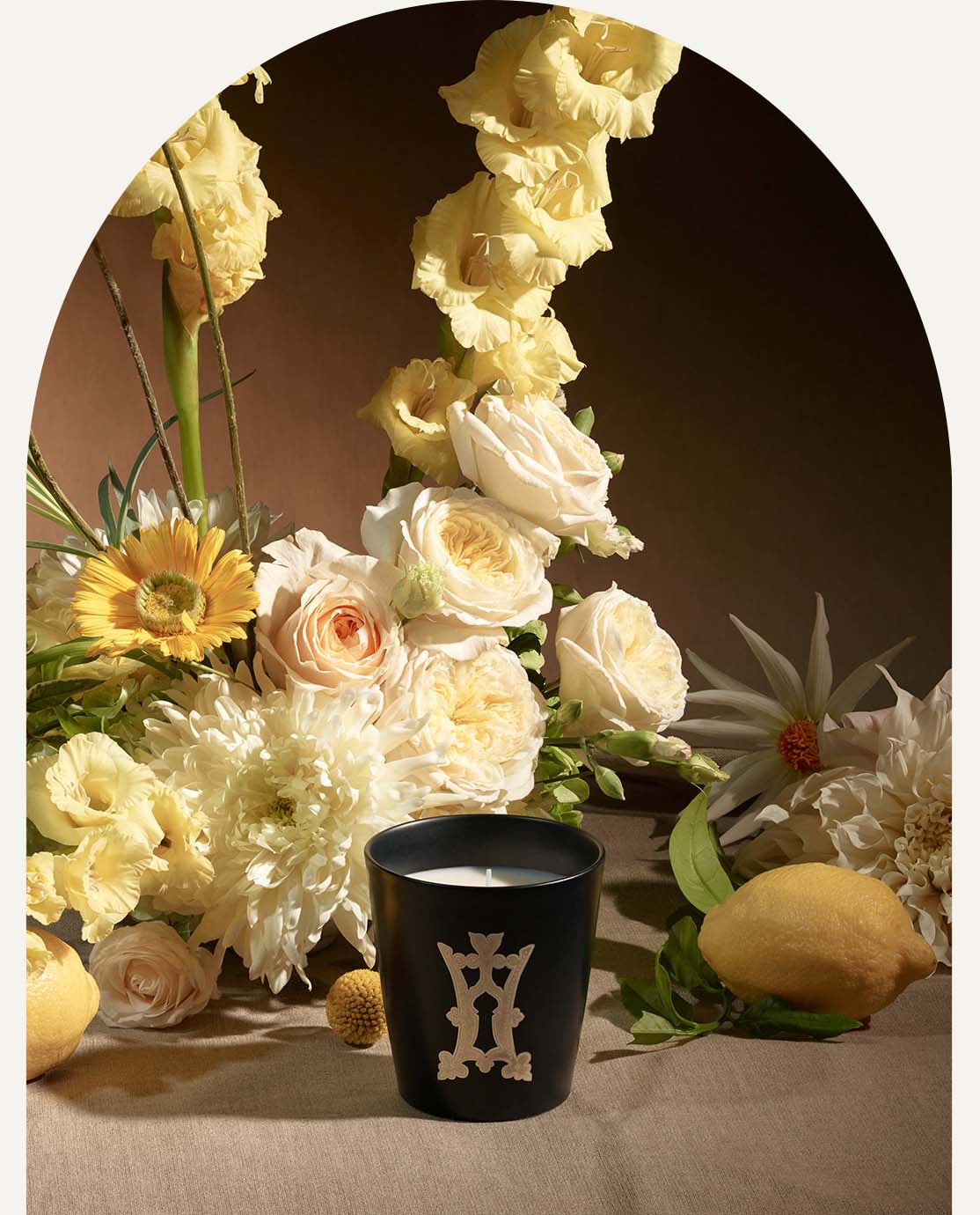 A black candle in front of a lemon and a bouquet of yellow flowers