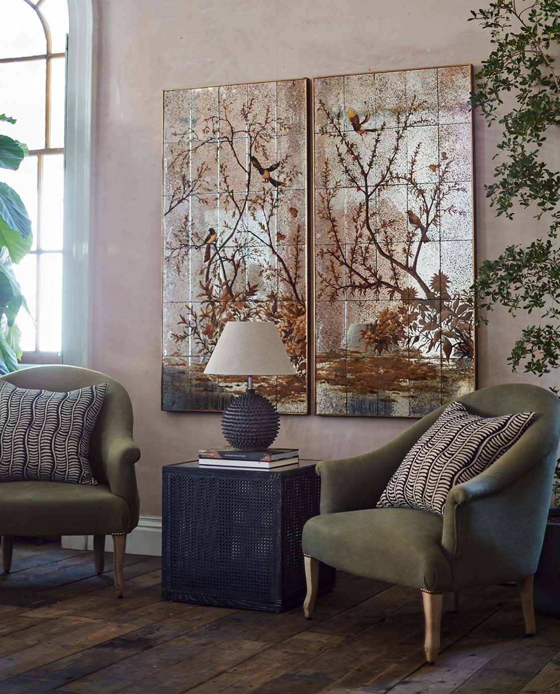 Two mirrored artworks hang above a pair of green armchairs