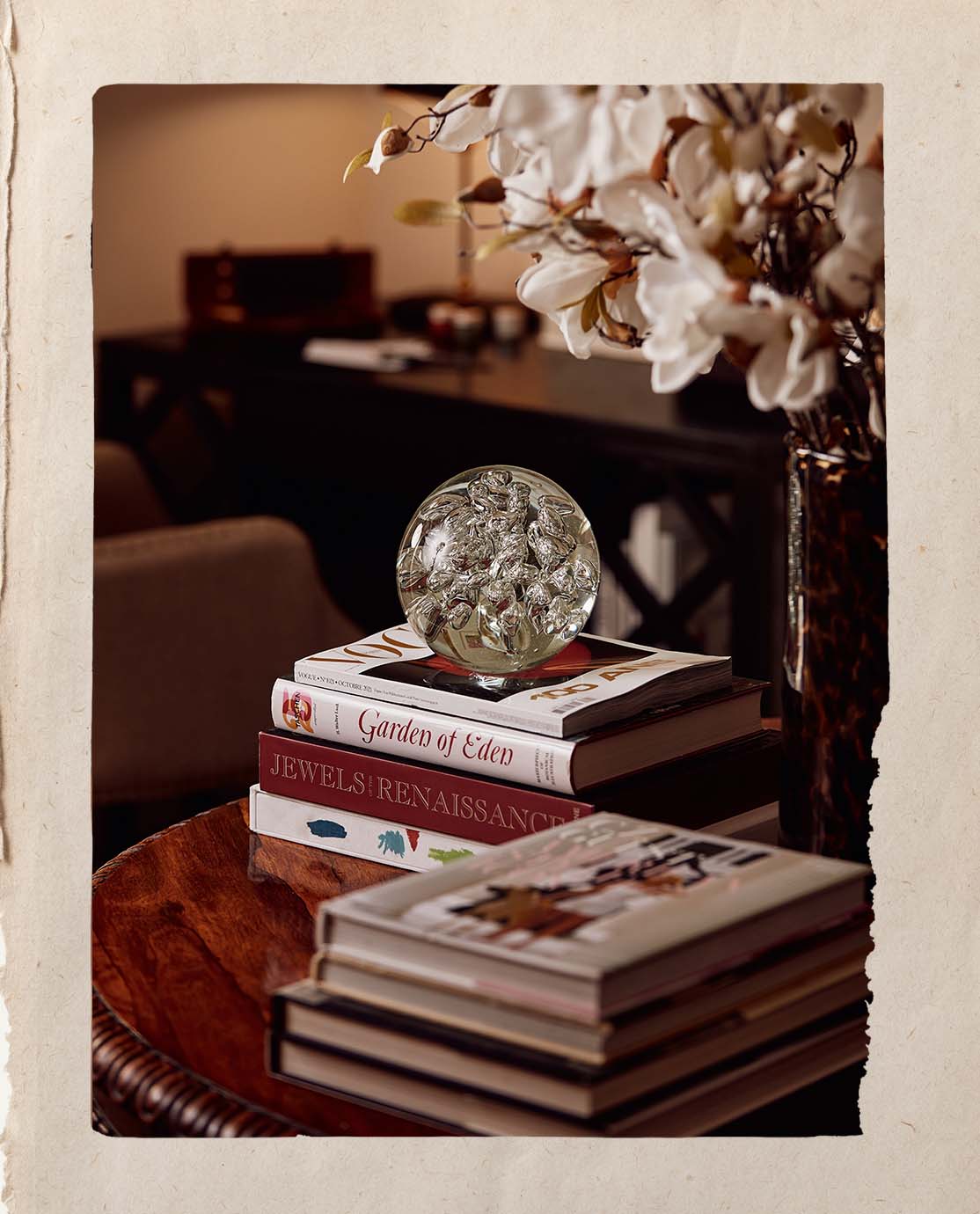 A side table decorated with coffee table books, a glass ball paperweight and a tortoiseshell vase with pink flowers