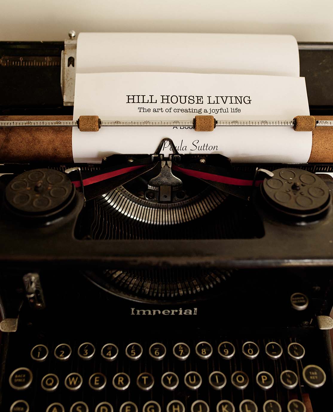 A close-up of a type-writer. A piece of paper is in it with "Hill House Living: The Art of Creating a Joyful Life" written on it