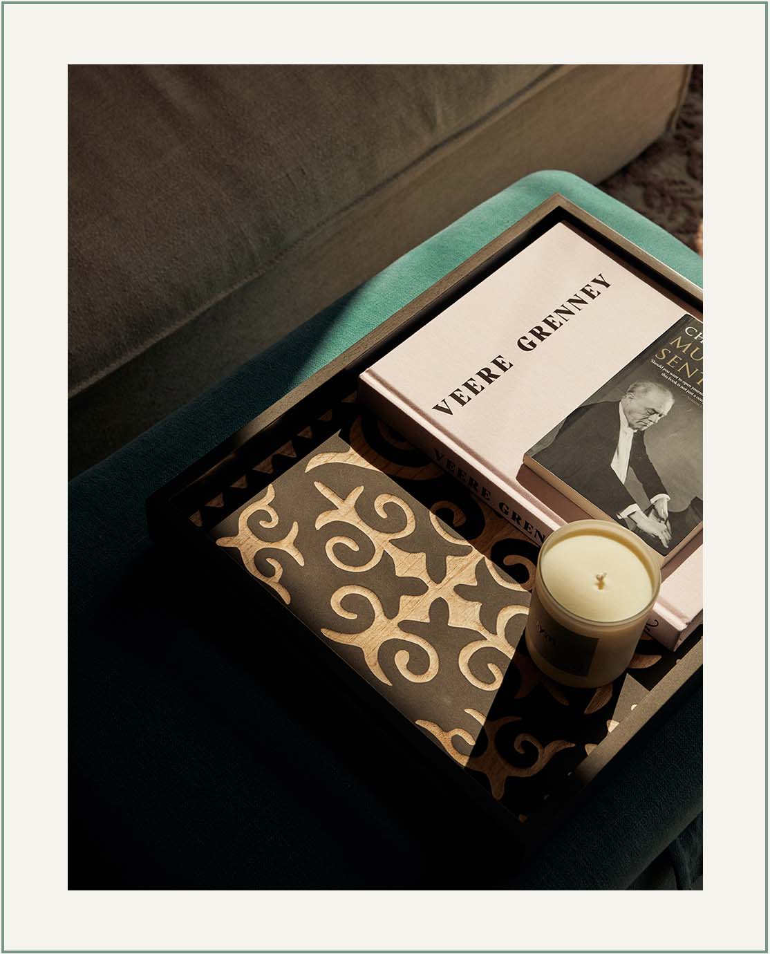 A wooden carved tray decorated with a candle and a coffee table book