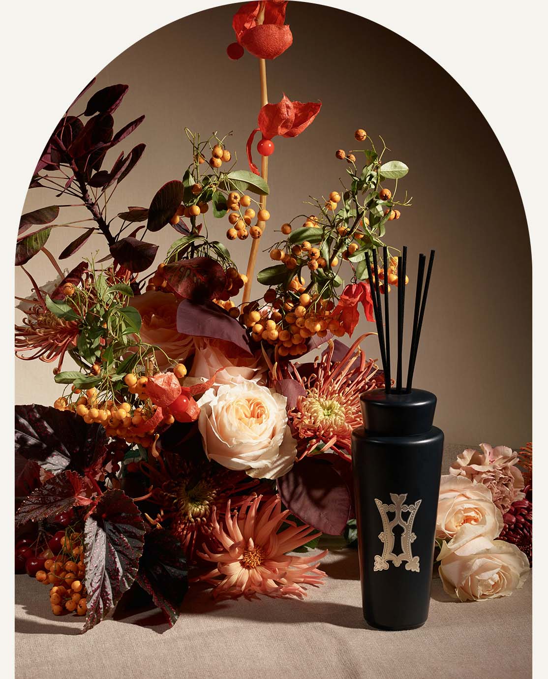 A black diffuser in front of a bouquet of orange and red flowers