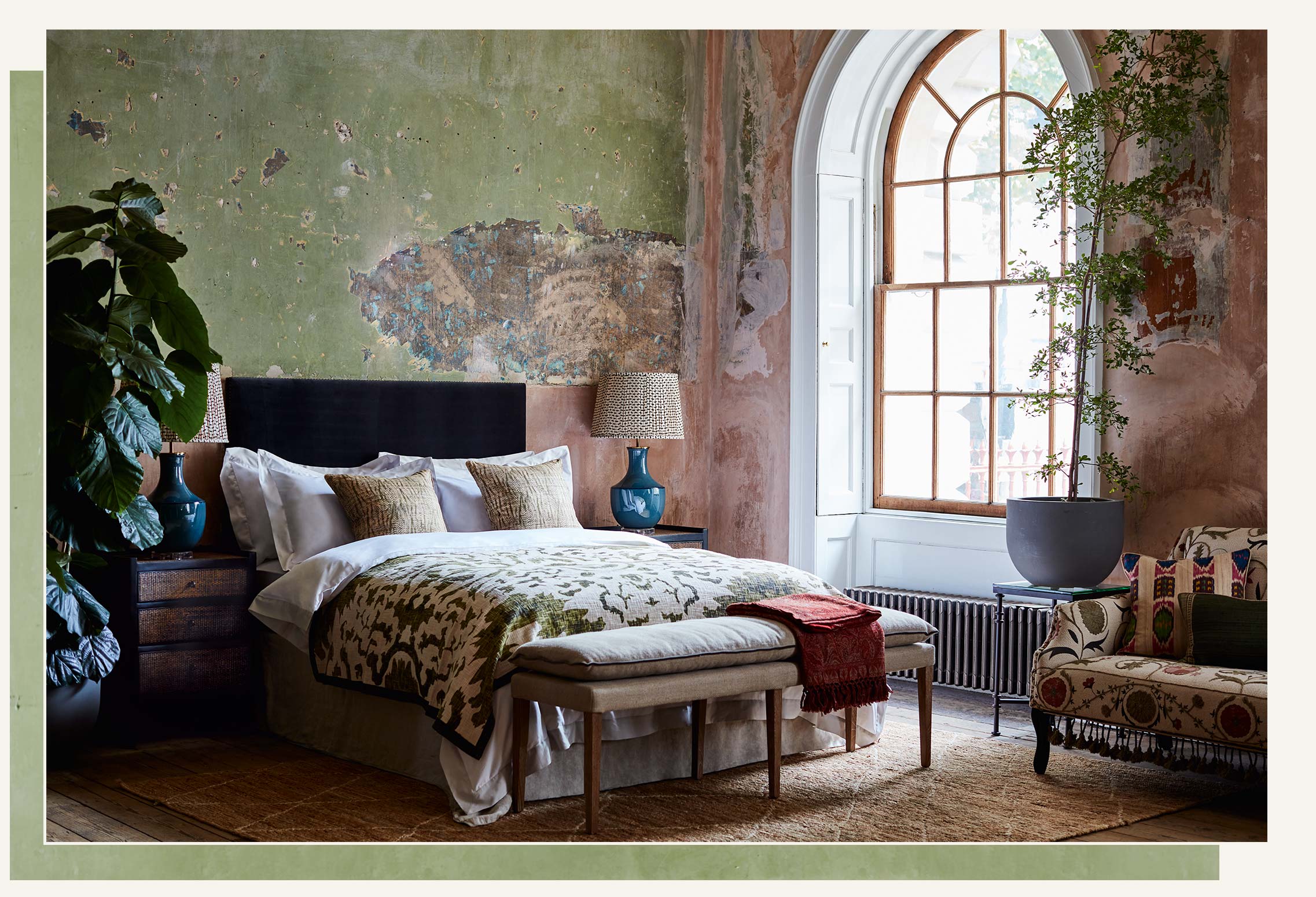 A bedroom setting with distressed walls, a bed with a patterned throw and an upholstered bench.