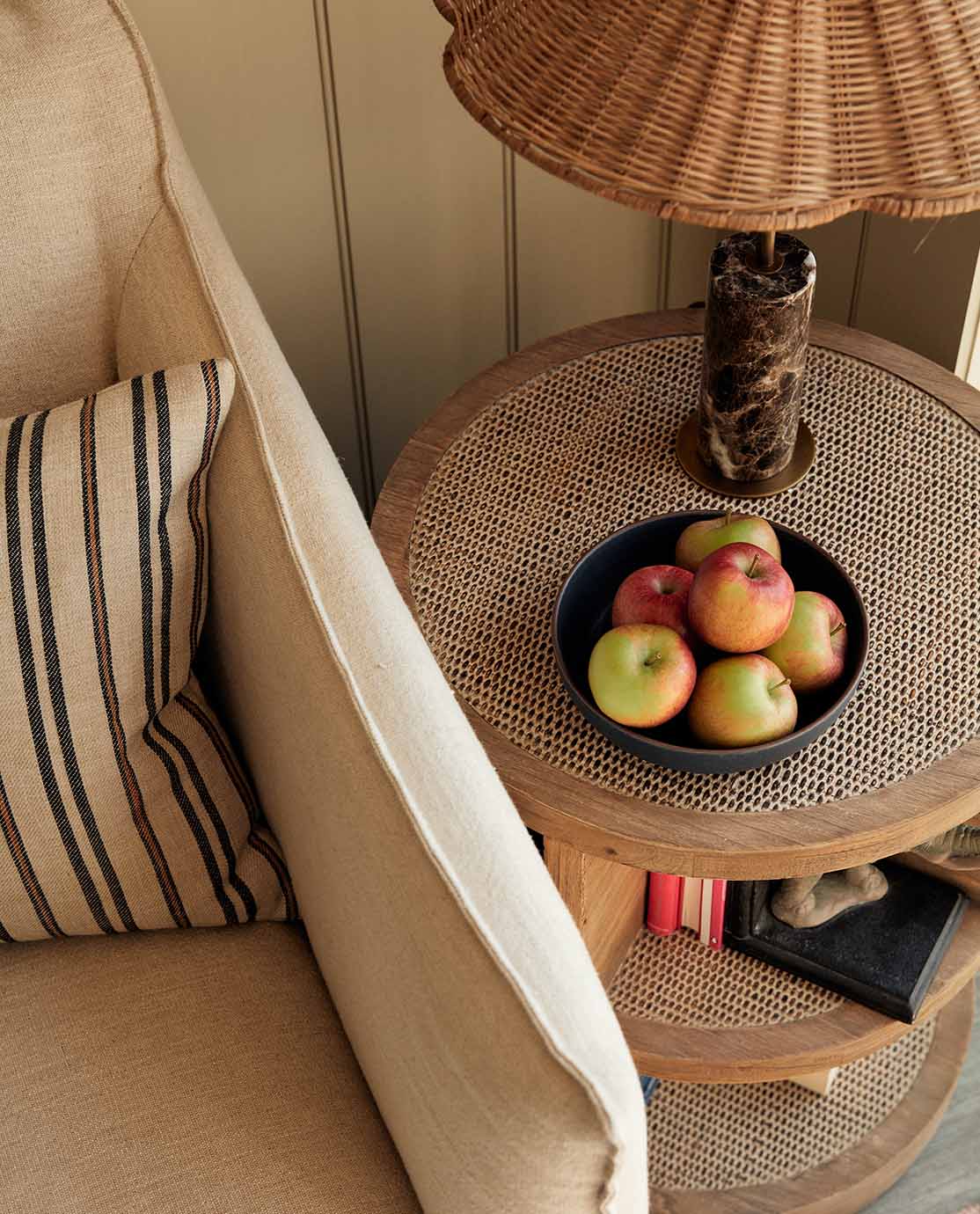 A linen-covered armchair and striped cushion sits next to a wooden and cane side table