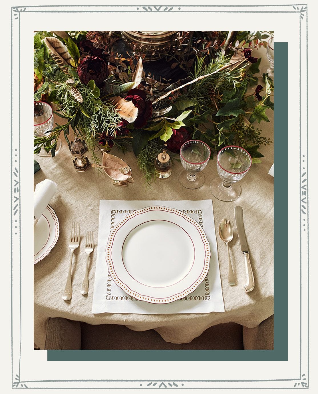 A close up of a a dining table decorated for Christmas with foliage, glassware, white crockery and napkins