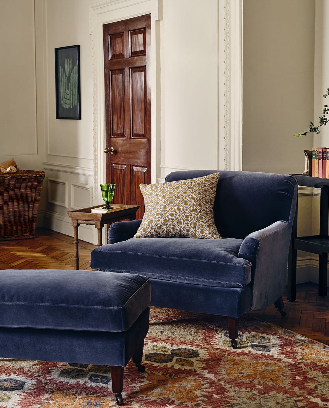 A blue velvet armchair and matching footstool, decorated with a patterned cushion.