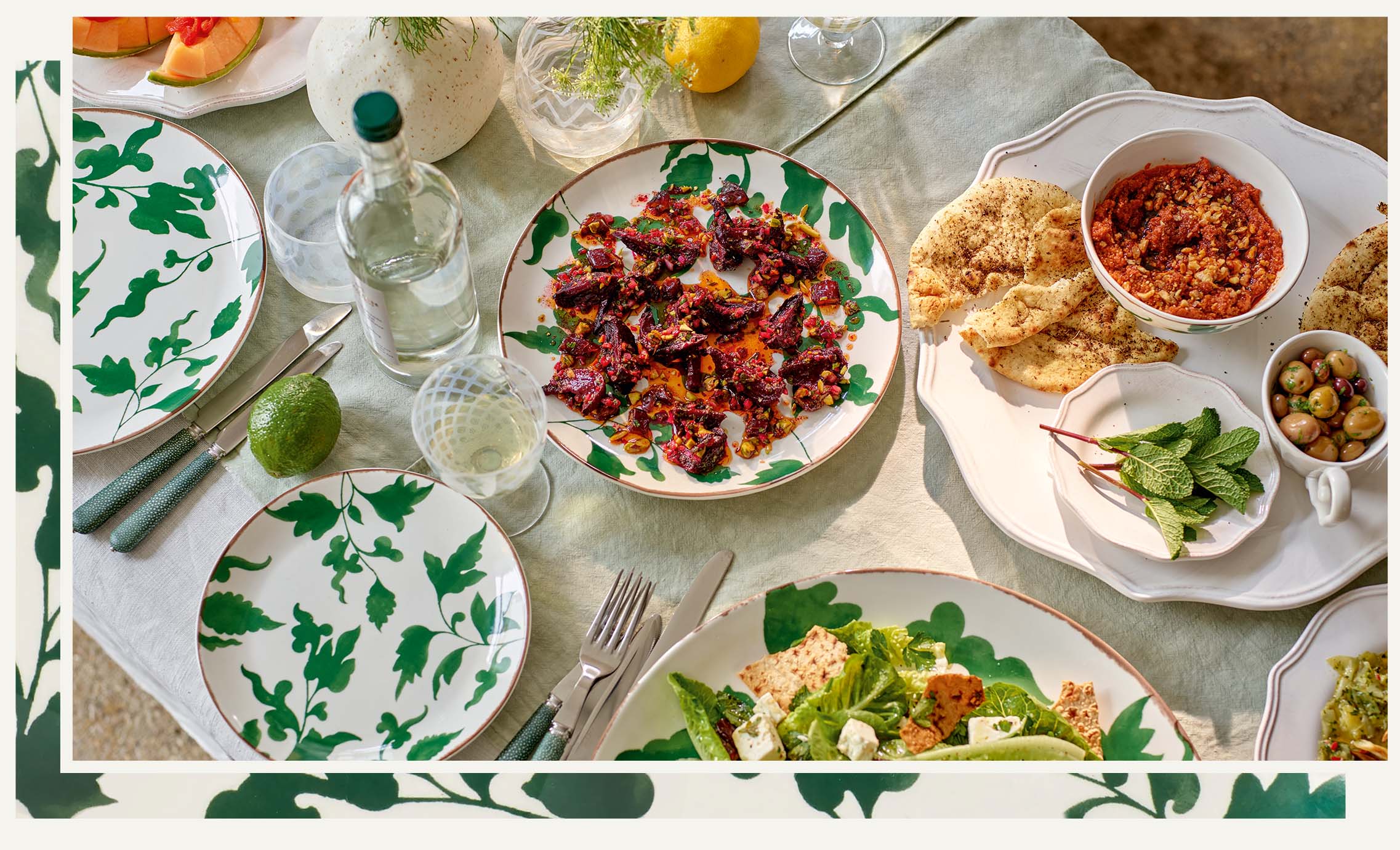 A meze spread of dishes on a table set with leaf-patterned plates, printed glassware and white napkins.