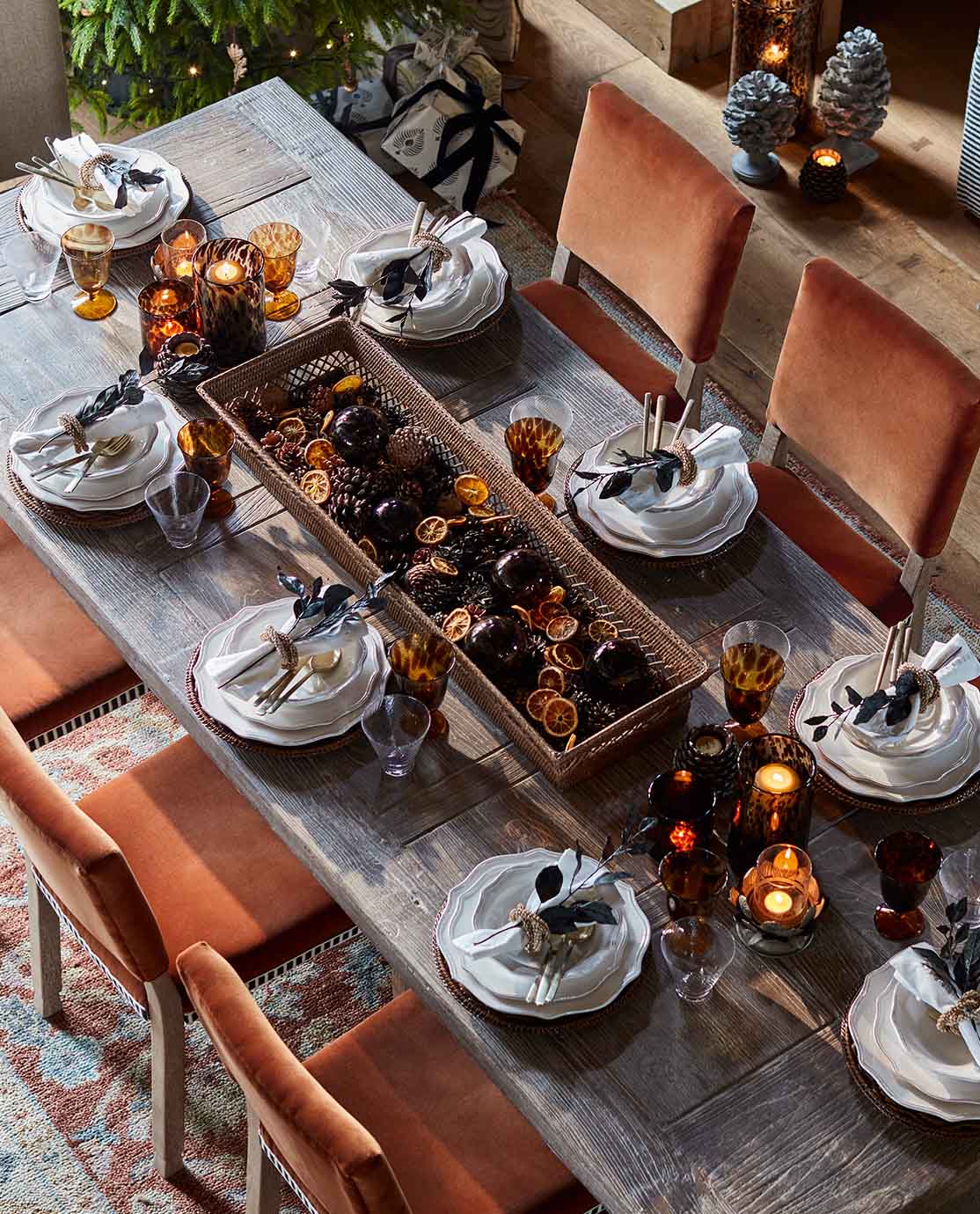 An aerial shot of a festive dining table, decorated with a pine cone centrepiece and surrounded by orange velvet chairs.