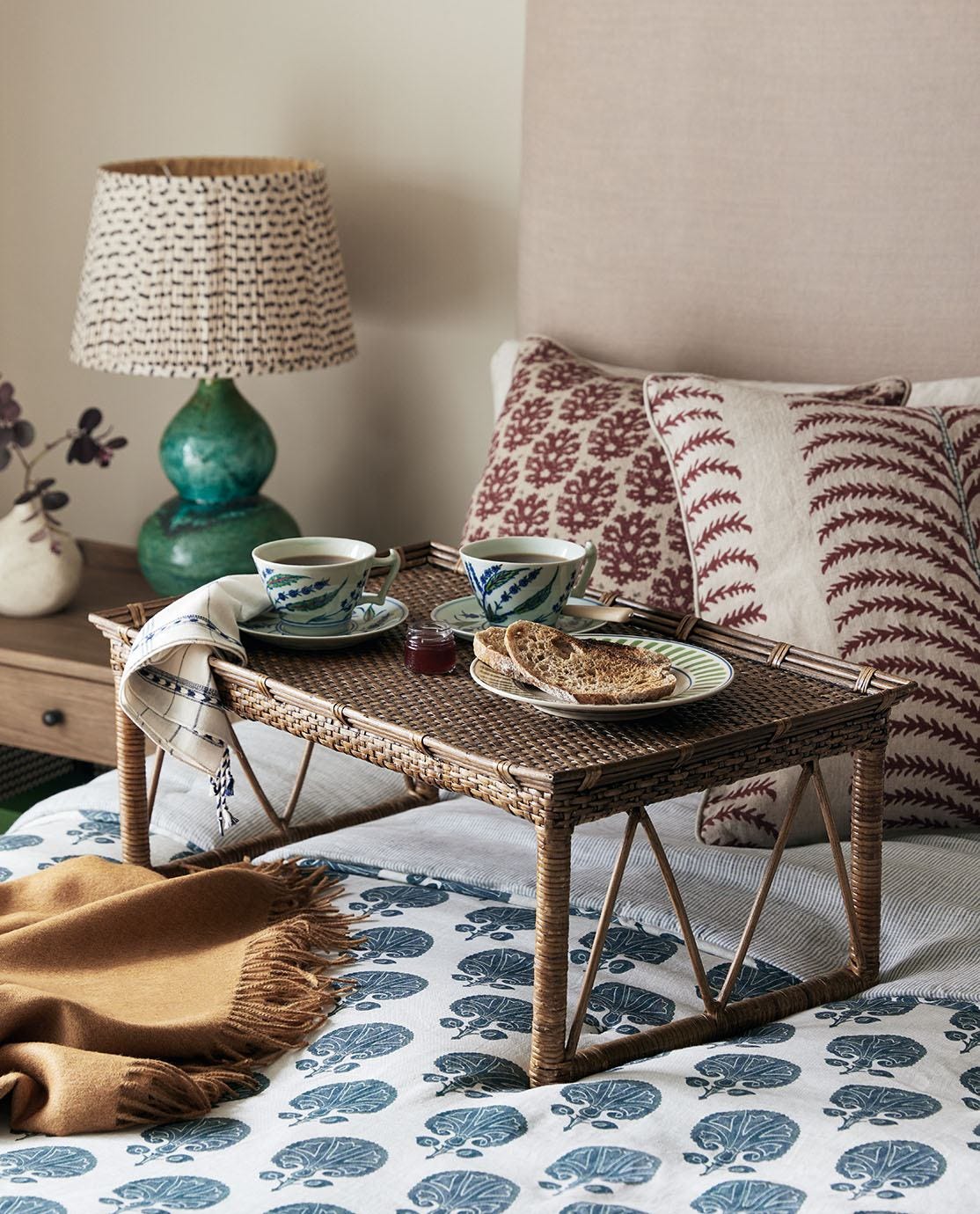 The Minyas Bed Tray stood on a bed, serving breakfast and tea, surround by quilts, cushions and a throw
