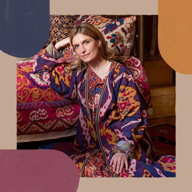 Martina Mondadori is sitting on the floor wearing a bright abstract patterned dress leaning with on a red patterned sofa.