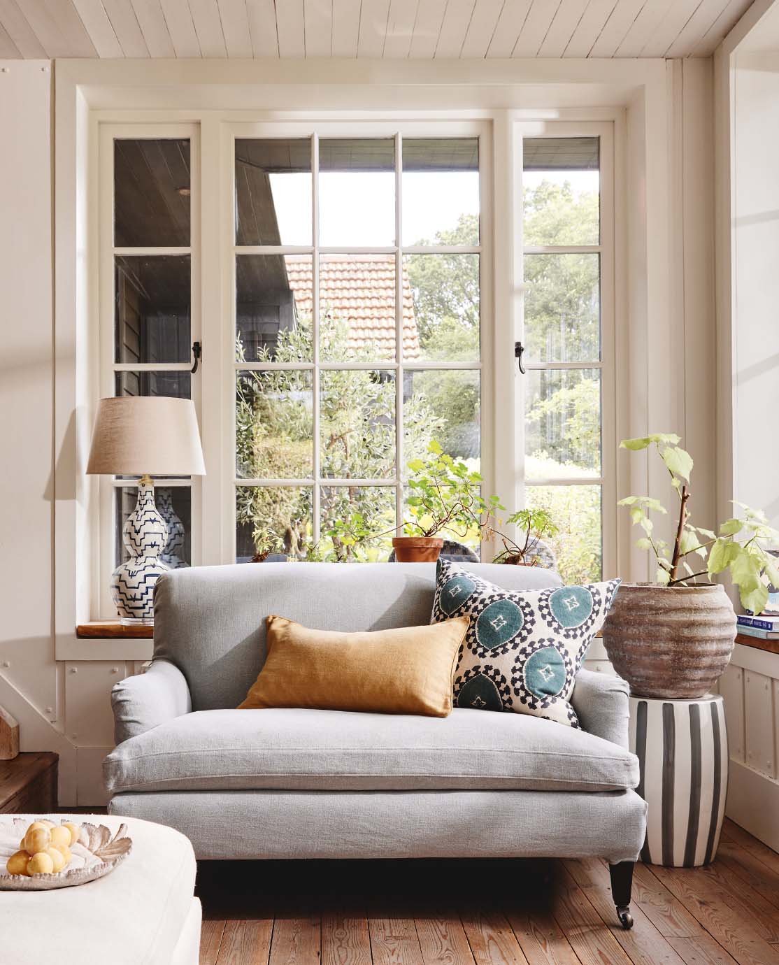 A cottage sitting room setting, with a light blue sofa, yellow and blue cushions and a blue lamp.