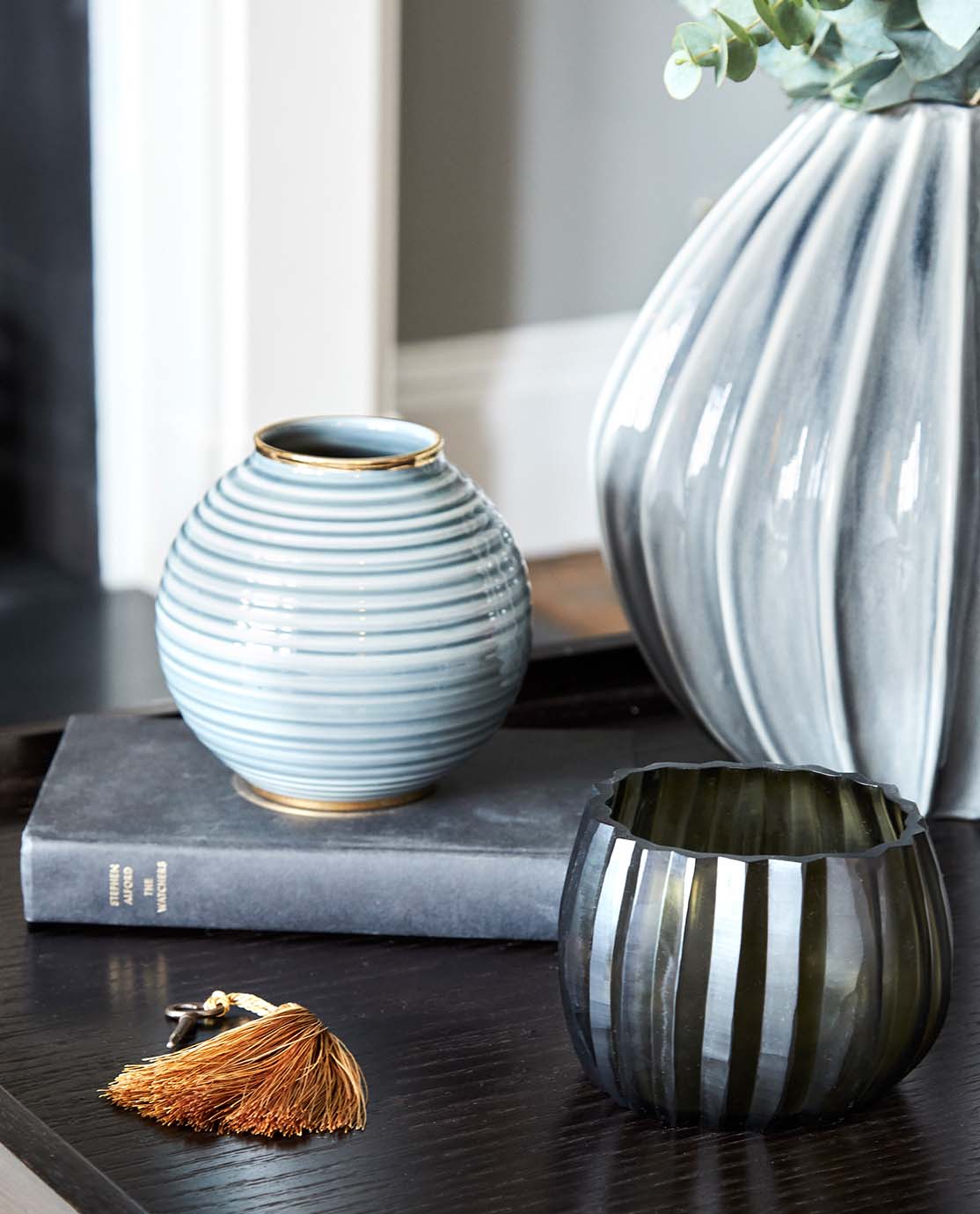 Blue pots, a book and an amber tasselled key ring sit on the edge of a black table.
