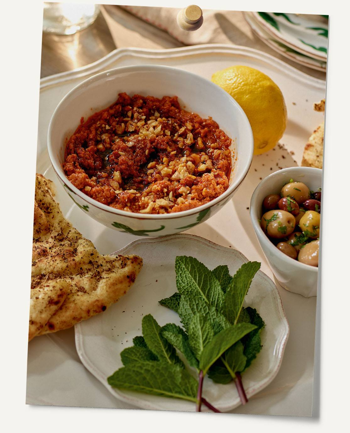 A traditional Turkish dip presented in a white bowl. Some bread and a bowl of olives sits next to it.