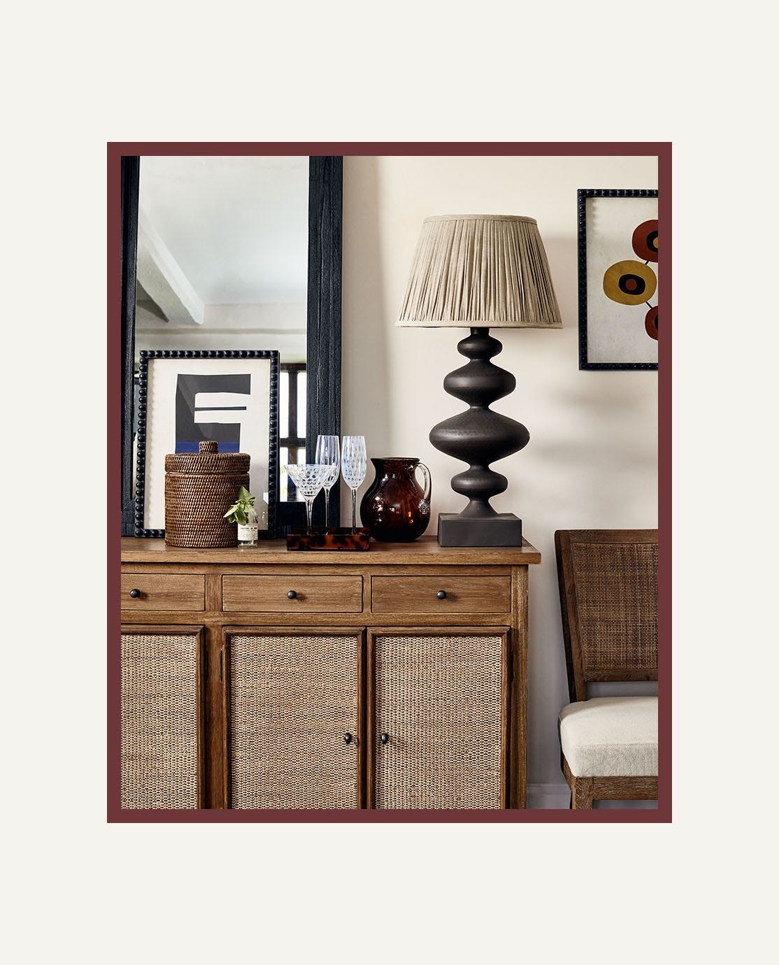 A wooden cabinet featuring wicker doors, with a black sculptural lamp and ornaments sat on top of it.