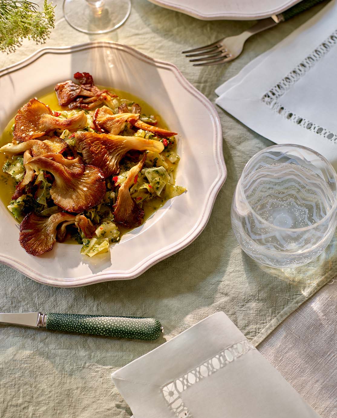 An oyster mushroom and leek dish on a white plate, with white napkins and faux shagreen cutlery