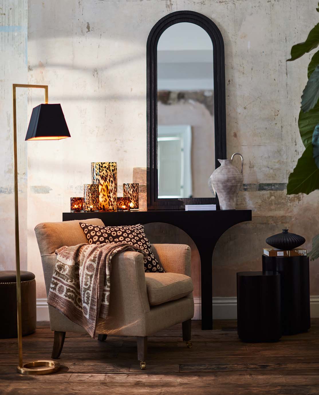 A cosy sitting room corner, with a sculptural gold floor lamp, beige armchair and tortoiseshell candles.