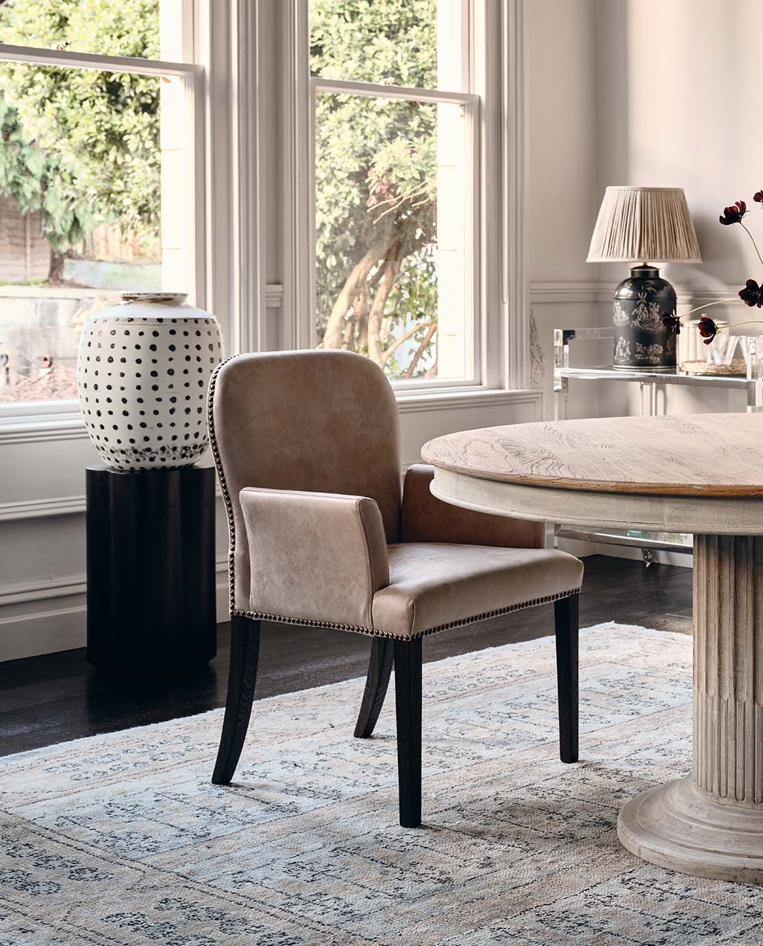 A round dining table with a column-style pedastal and a leather dining chair sit on a Persiasn-style beige and mint green rug