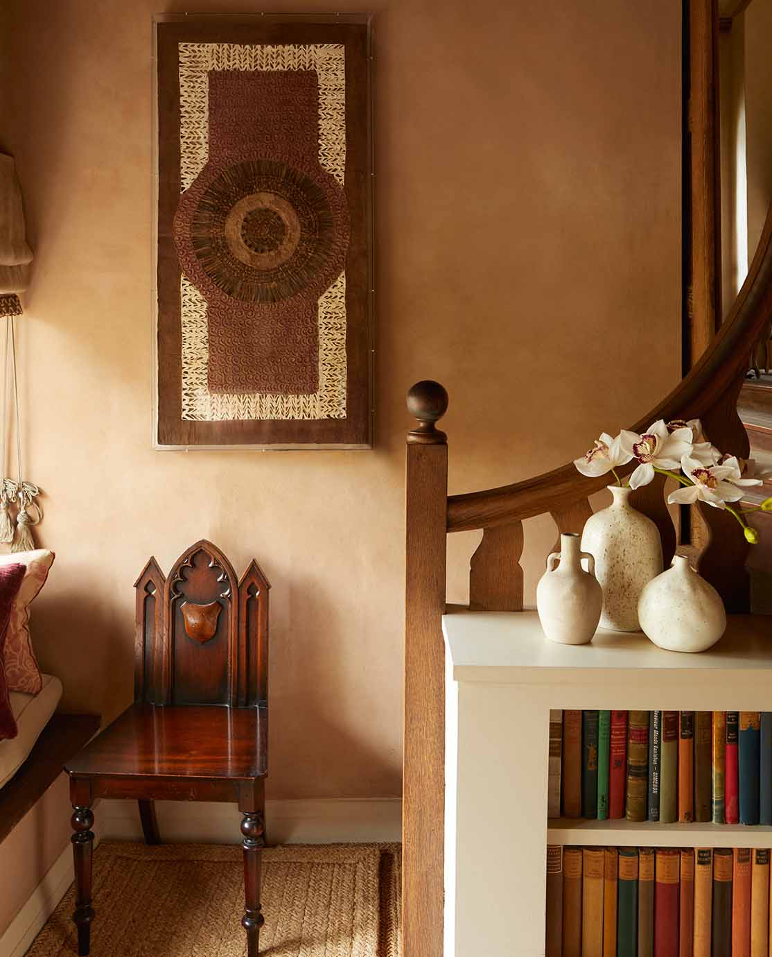 An antique chair and textural wall art sit at the bottom of a wooden staircase.