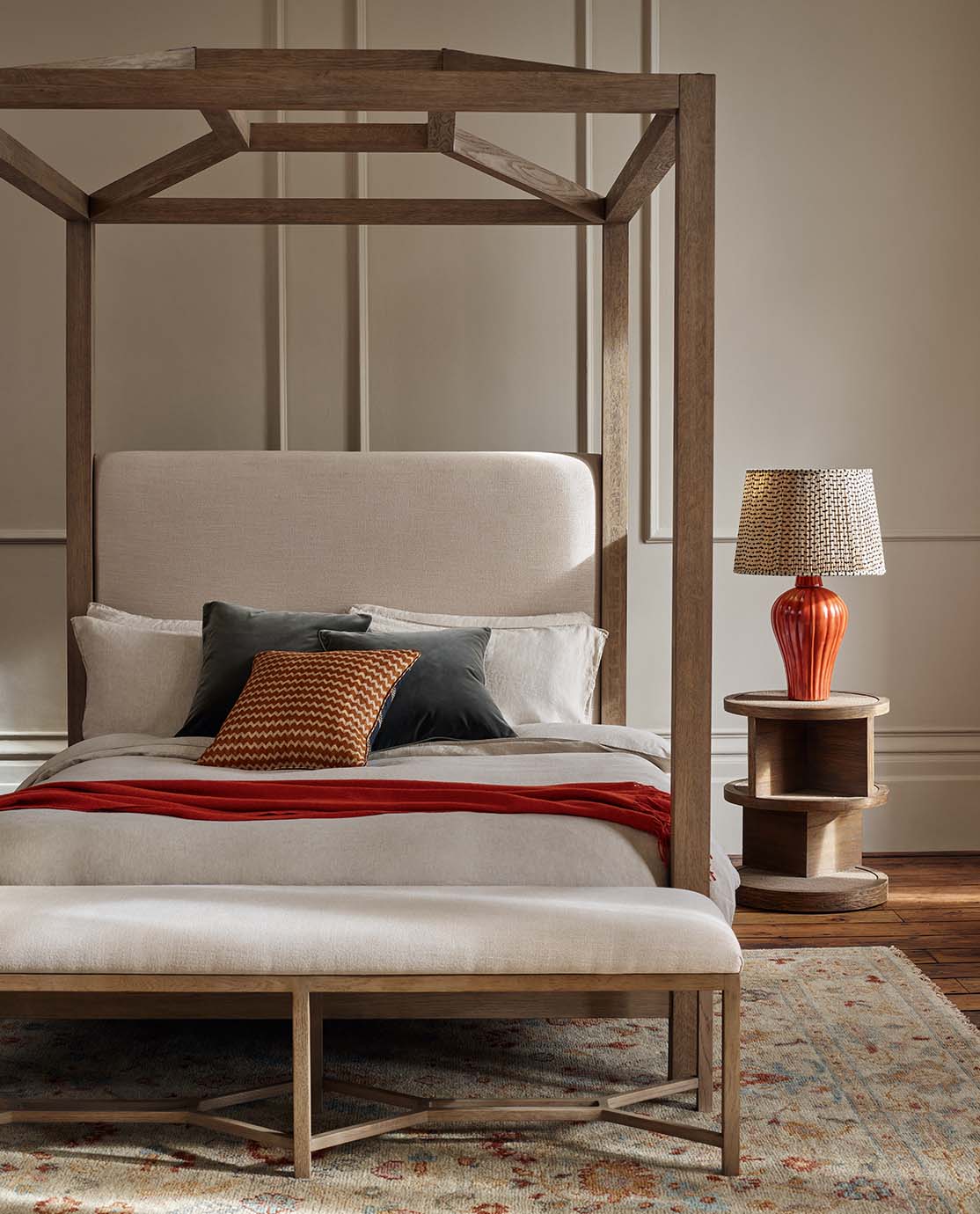 Bedroom with wooden four poster bed with cushions, a bench and a lamp